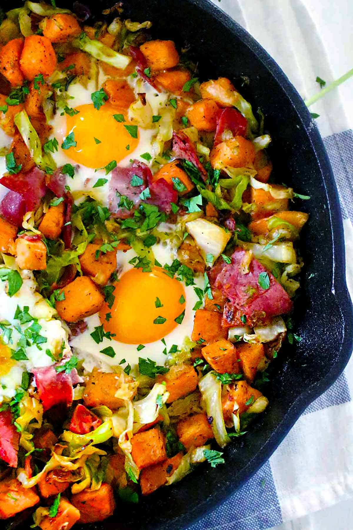 Overhead close up photo of cabbage, sweet potatoes, corned beef, and eggs in a cast iron skillet.