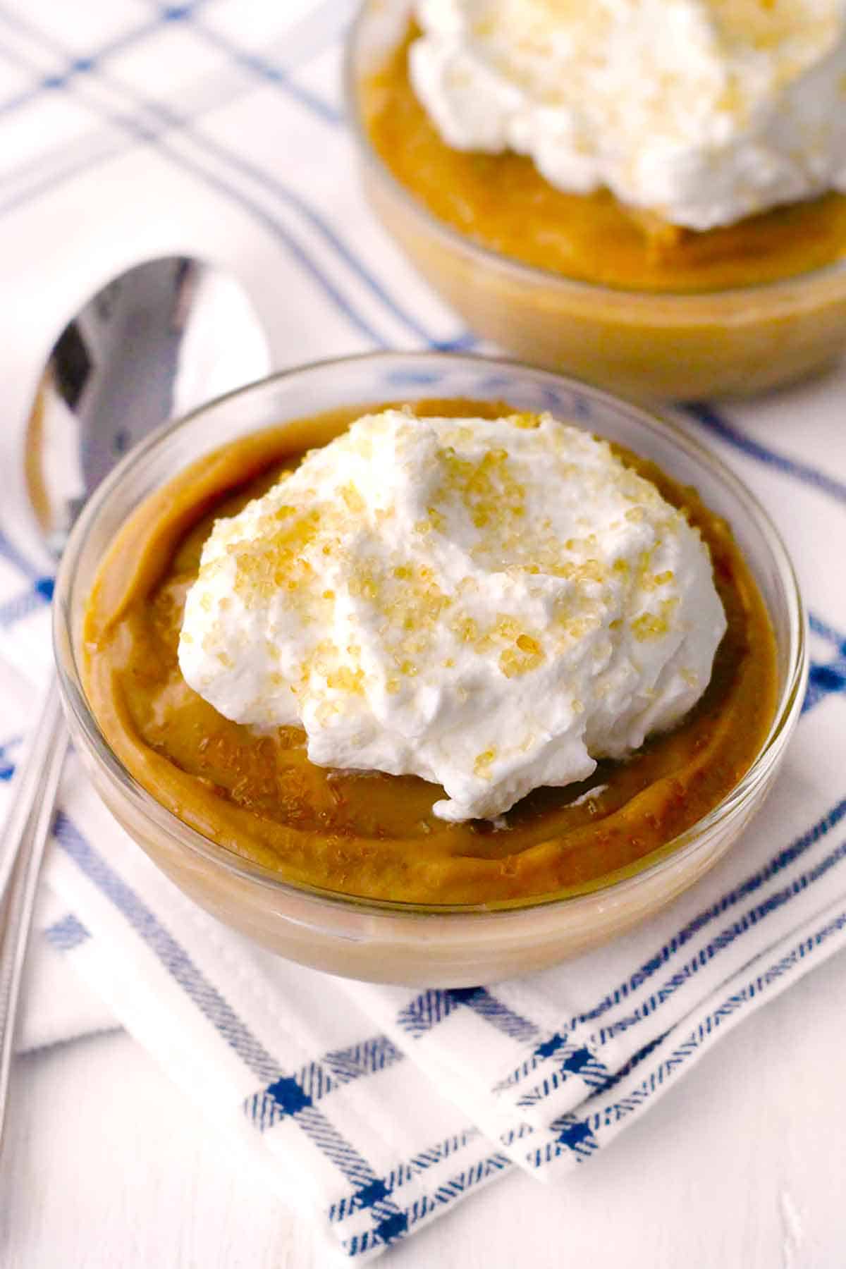 Close up photo of a bowl of butterscotch pudding with whipped cream and sugar on top.
