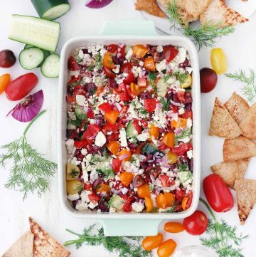 This Mediterranean Seven-Layer Dip recipe is fresh and delicious! It's the perfect snack to serve with pita chips. No cooking required! It's packed with hummus, fresh veggies, olives, and feta and it's super easy to assemble. #MediterraneanDiet #Vegetarian #Appetizers #NoCookRecipes #SevenLayerDip #GlutenFreeSnacks