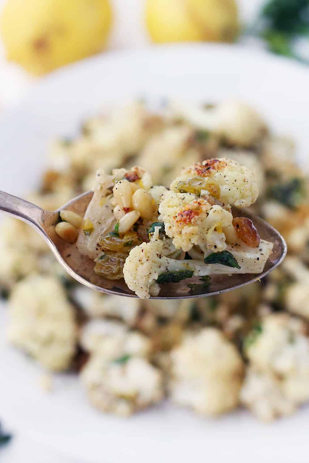 This roasted cauliflower with pine nuts and raisins is a delicious side dish served warm or cold. Tossed with a lemon and olive oil vinaigrette and fresh parsley, it's a fresh Mediterranean recipe that goes with just about anything! Capers or olives can be substituted for raisins for a saltier, lower carb version.