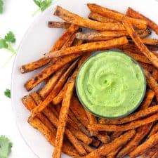 These crispy baked sweet potato fries are coated in chili powder, garlic, and a light coat of corn starch, which helps to make them crispy! Perfect for dipping into the cool, smooth, and creamy avocado cilantro sauce.