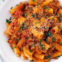 Square overhead close up photo of a bowl of rigatoni with bolognese sauce, showing how the texture of the sauce clings to each piece of pasta.
