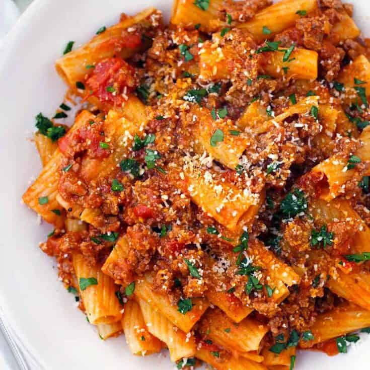 Square overhead close up photo of a bowl of rigatoni with bolognese sauce, showing how the texture of the sauce clings to each piece of pasta.