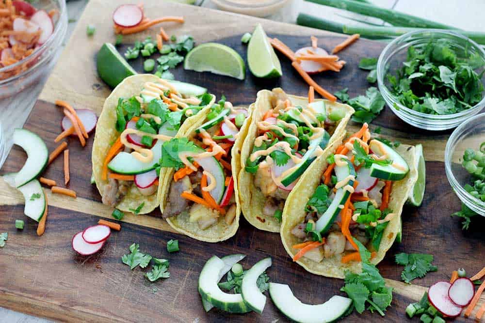 Chicken Banh Mi Tacos are bursting with fresh Vietnamese flavor. Marinated chicken thighs and pickled veggies, wrapped in toasted corn tortillas, topped with a spicy mayo and cool cucumber and herbs! This is an easy, gluten free recipe.