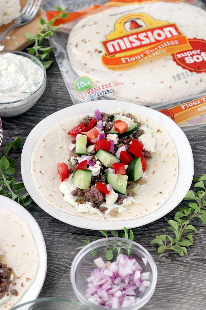 An open Greek lamb taco on a flour tortilla.