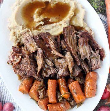 A platter with pot roast, mashed potatoes, carrots, and gravy overhead shot