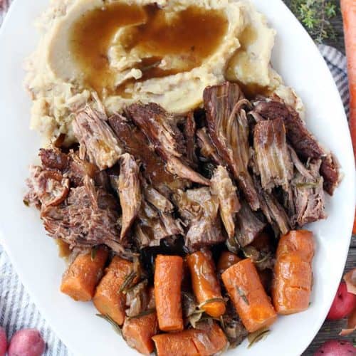 A platter with pot roast, mashed potatoes, carrots, and gravy overhead shot