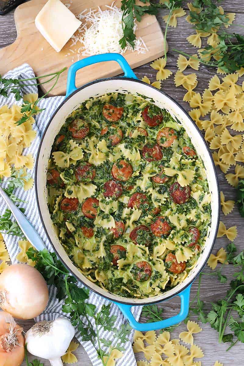 Over head photo of a Dutch oven with pasta, sausage, and spinach and ingredients scattered around.