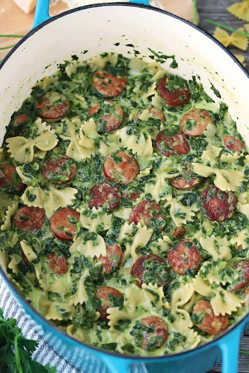 One pot pasta with sausage and spinach in a blue Dutch oven.