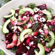A white bowl with beet salad with cucumbers, feta, and dill.