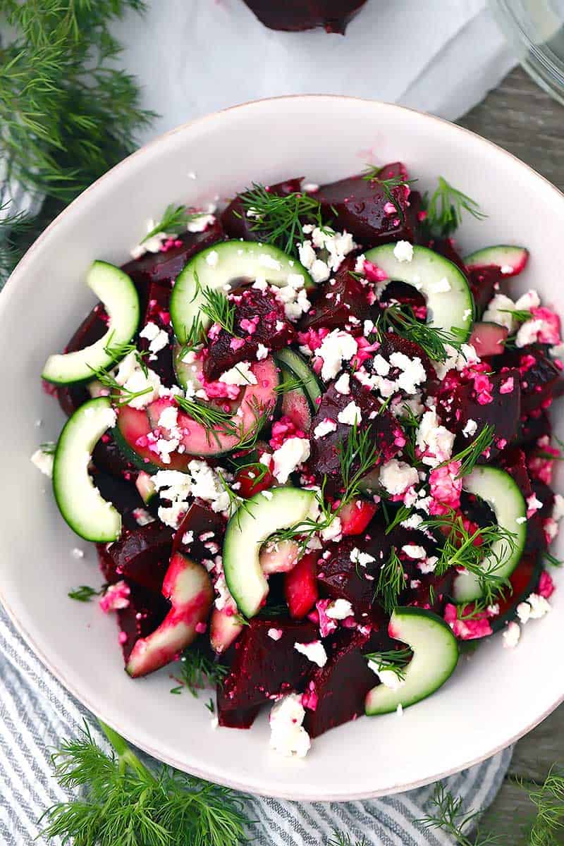 Beet, cucumber, and feta salad with fresh dill in a white bowl.