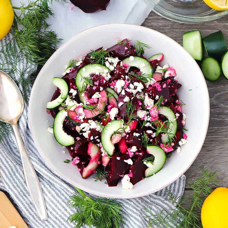 Square photo of a beet salad with fresh dill and lemons around it.