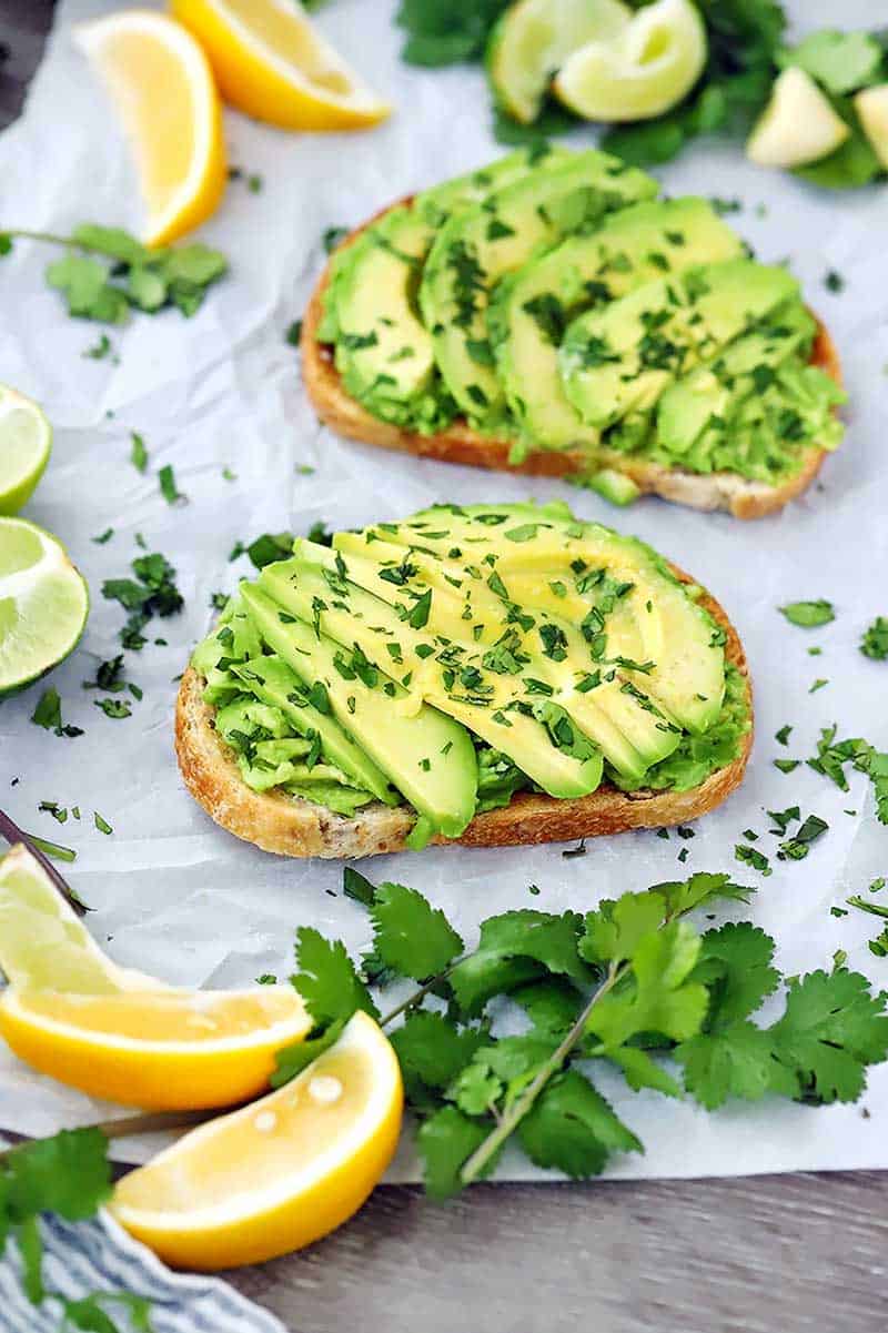 Avocado toast with cilantro and lemons scattered around.