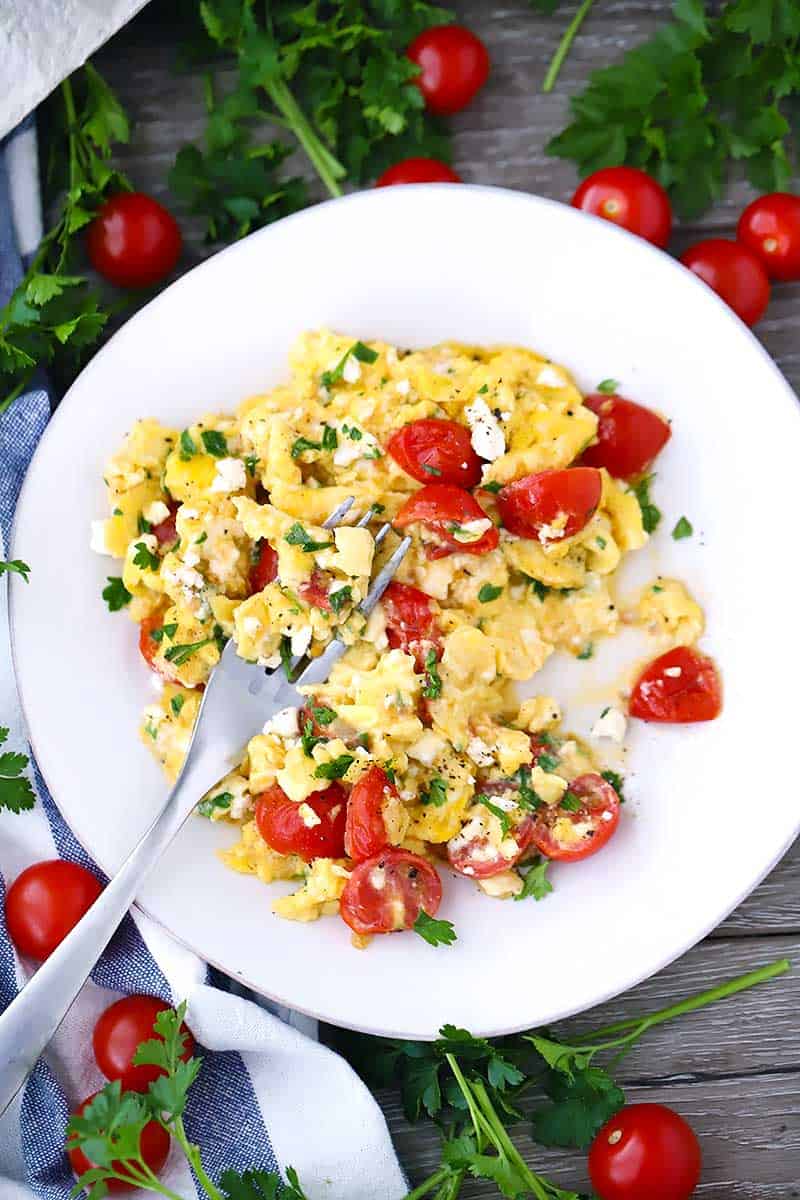 A fork on a plate with scrambled eggs and tomatoes and feta.