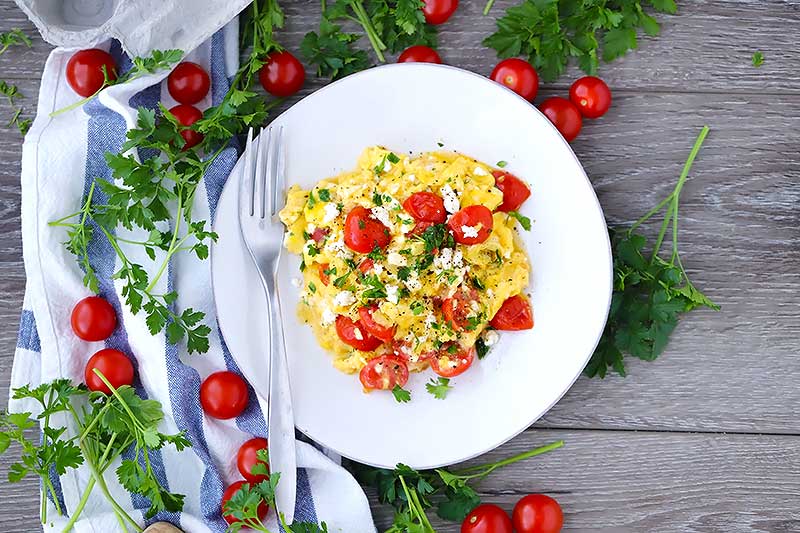 Overhead horizontal photo of a plate of scrambled eggs with feta and tomato.