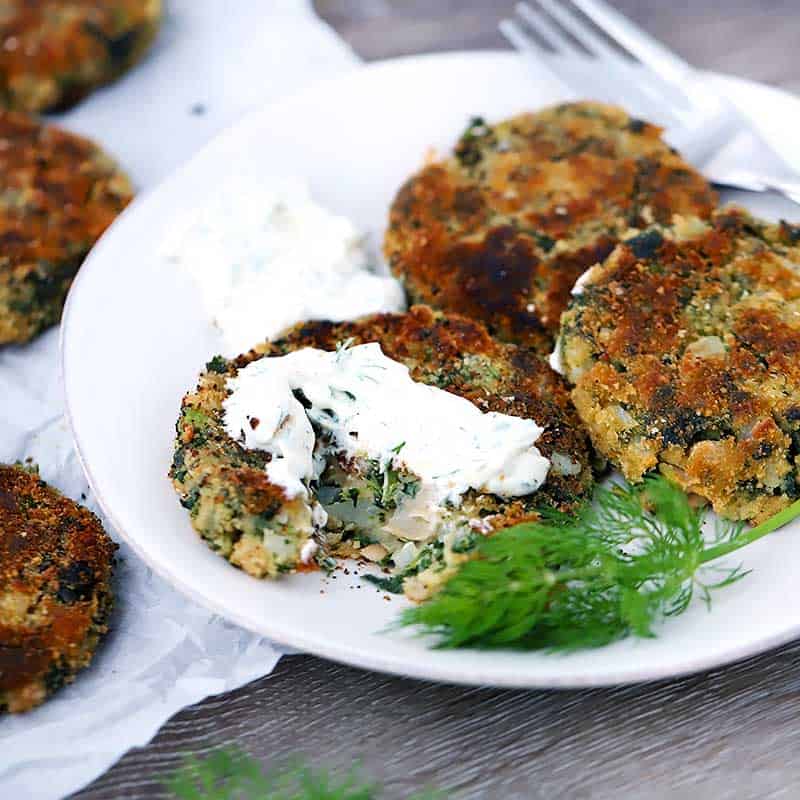 Square photo of white bean patties on a plate with yogurt sauce.