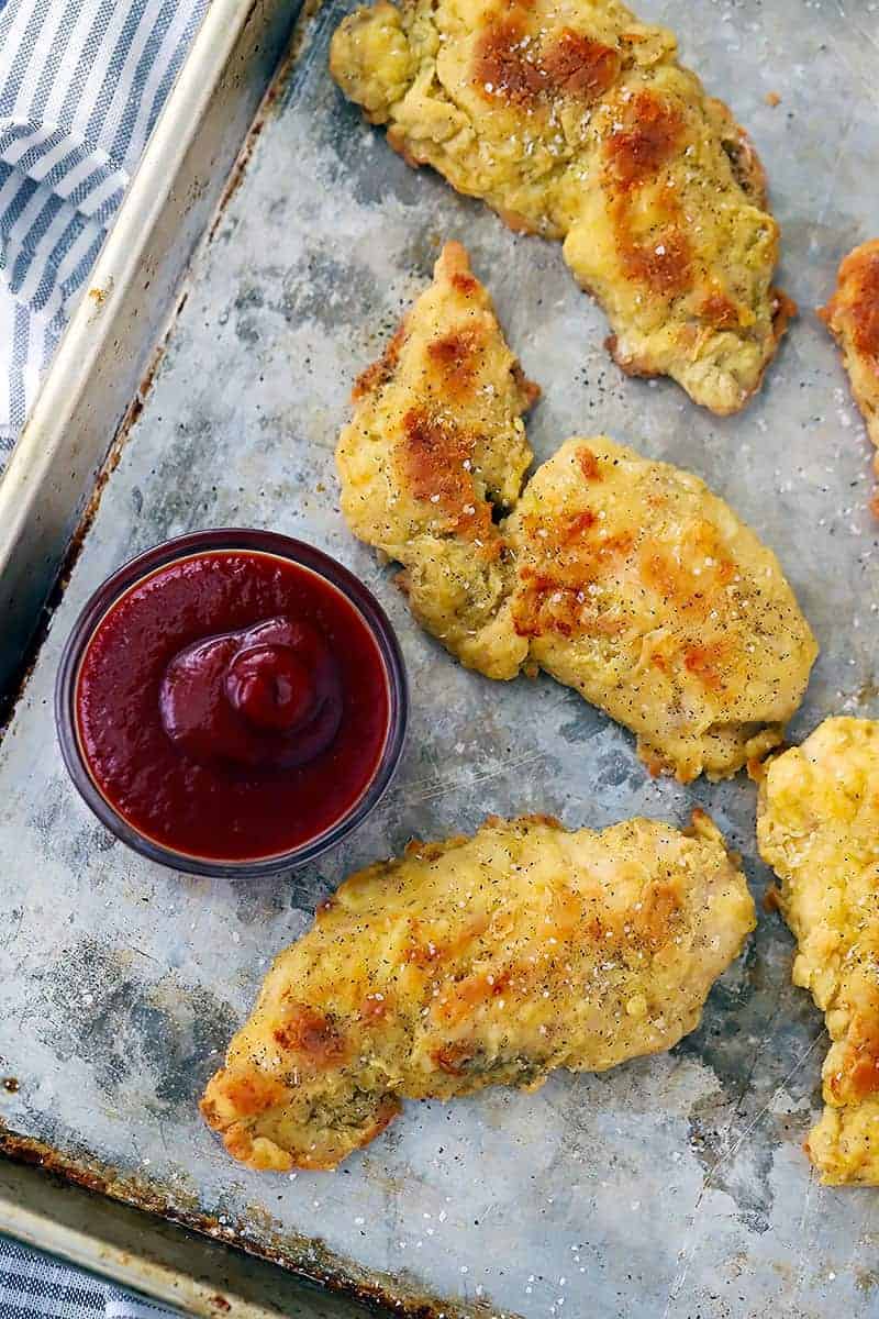 Chicken tenders on a baking sheet with ketchup.