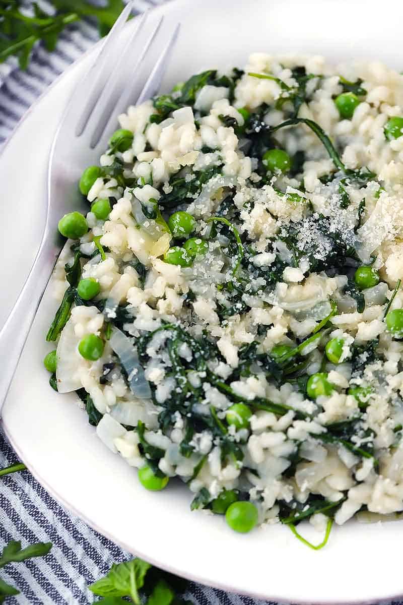 A close up overhead shot of risotto with peas, mint, and arugula on a plate with a fork.