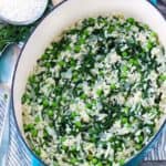 A blue dutch oven with fresh pea risotto with mint and arugula inside.