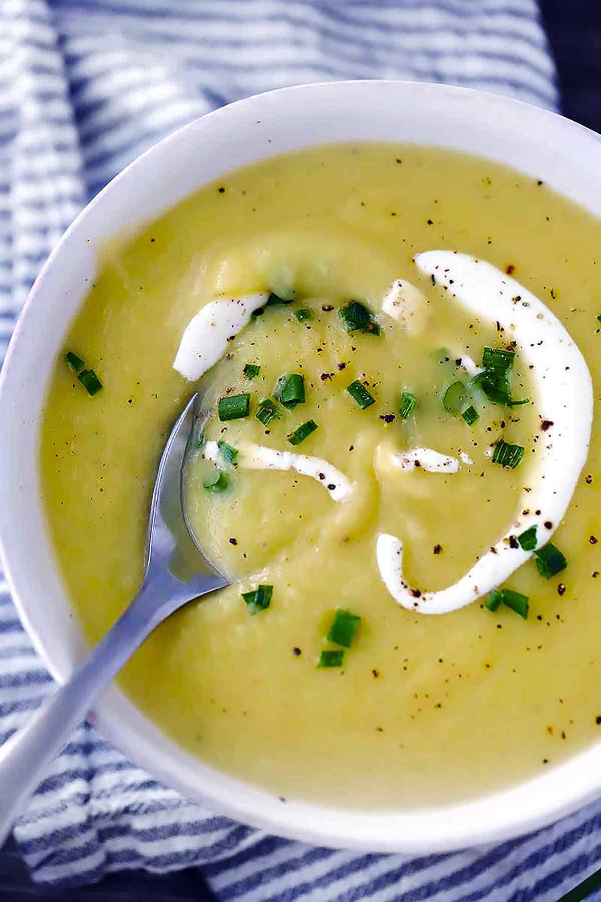 Close up overhead photo of potato leek soup with a spoon in a white bowl.