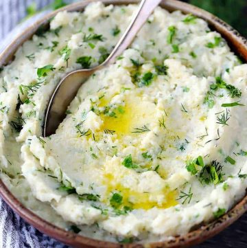 A bowl of mashed cauliflower with melted butter and fresh herbs and a spoon.