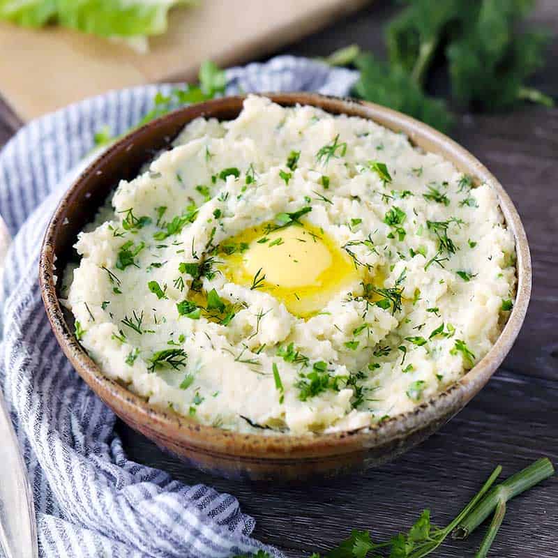 A bowl of mashed cauliflower with melted butter and fresh herbs.