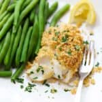 A square image of baked haddock with breadcrumb topping and green beans
