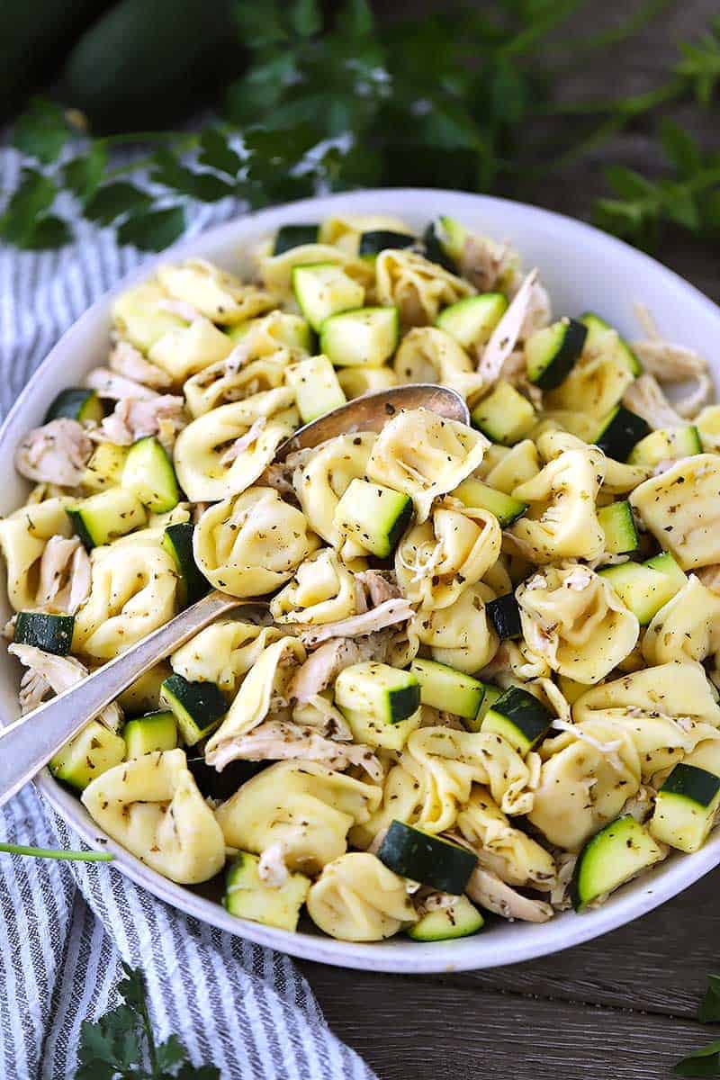 A close up photograph of Italian tortellini salad with shredded chicken and zucchini and a spoon.