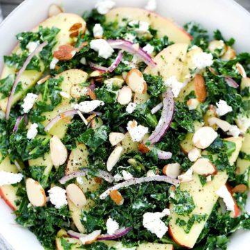 A close up overhead photo of a kale salad with apples and goat cheese.