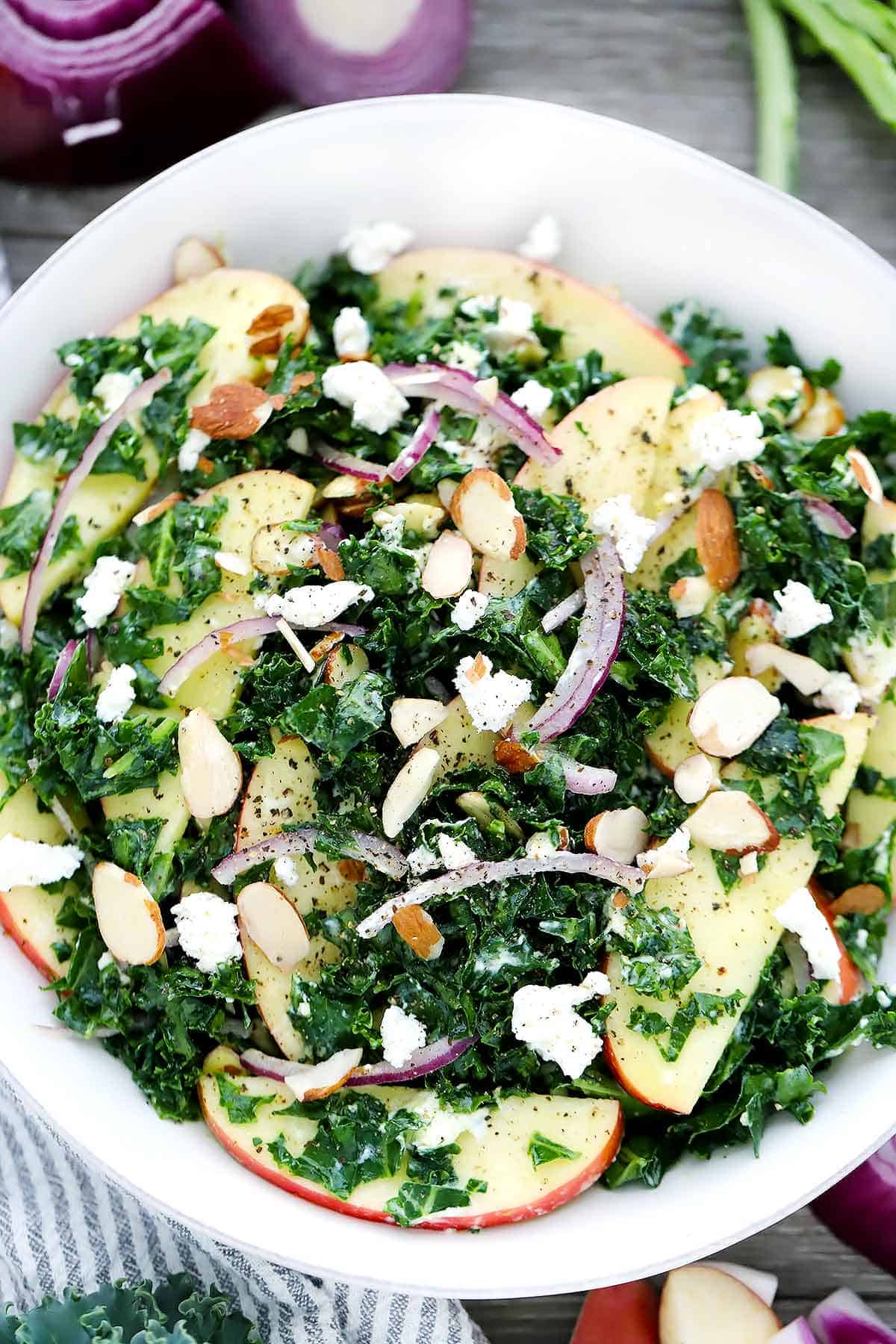 A close up overhead photo of a kale salad with apples and goat cheese.