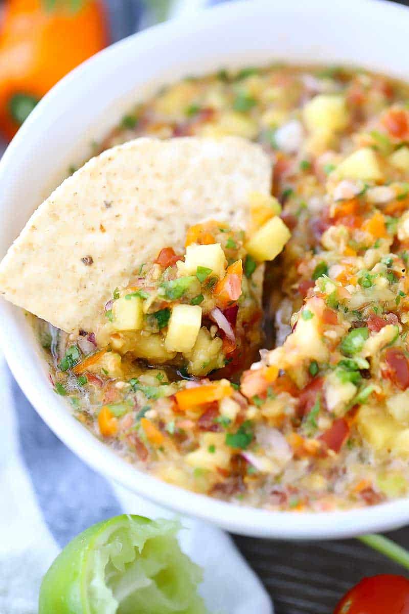 A close up bowl of pineapple salsa with a tortilla chip dipped in.