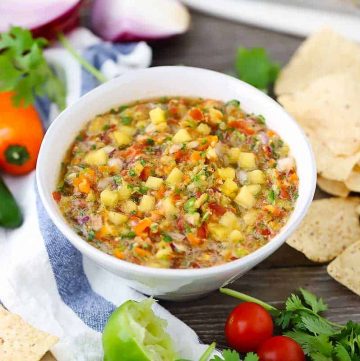 A bowl of pineapple salsa with tortilla chips in background.