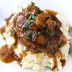 A close up of salisbury steak on top of mashed potatoes with mushroom gravy.