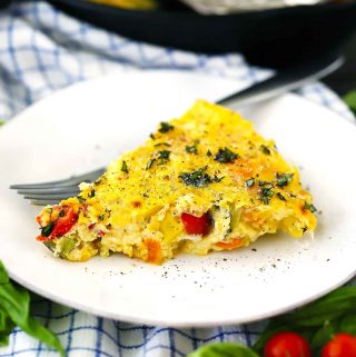 A slice of a frittata on a white plate with a fork.