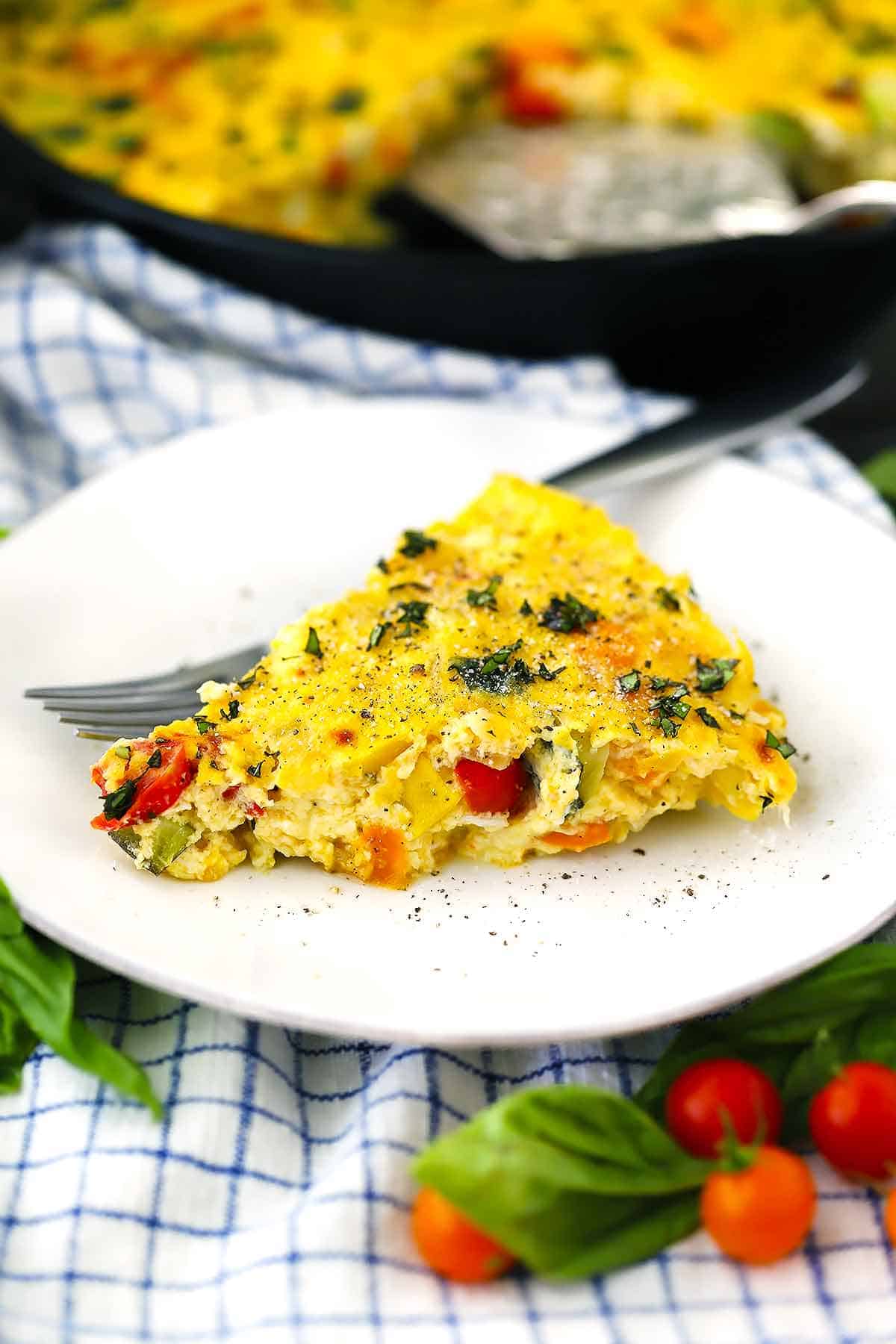 A slice of a frittata on a white plate with a fork.