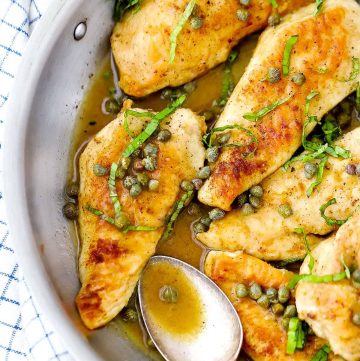 A close up photo of a chicken breast cutlet in a skillet with lemon butter caper sauce.