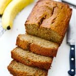 A sliced loaf of banana bread with bananas in the background.
