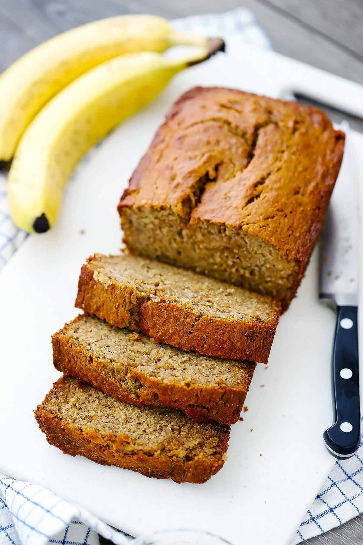 A sliced loaf of banana bread with bananas in the background.