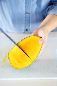 Using a knife to cut cubes of mango inside the peel.