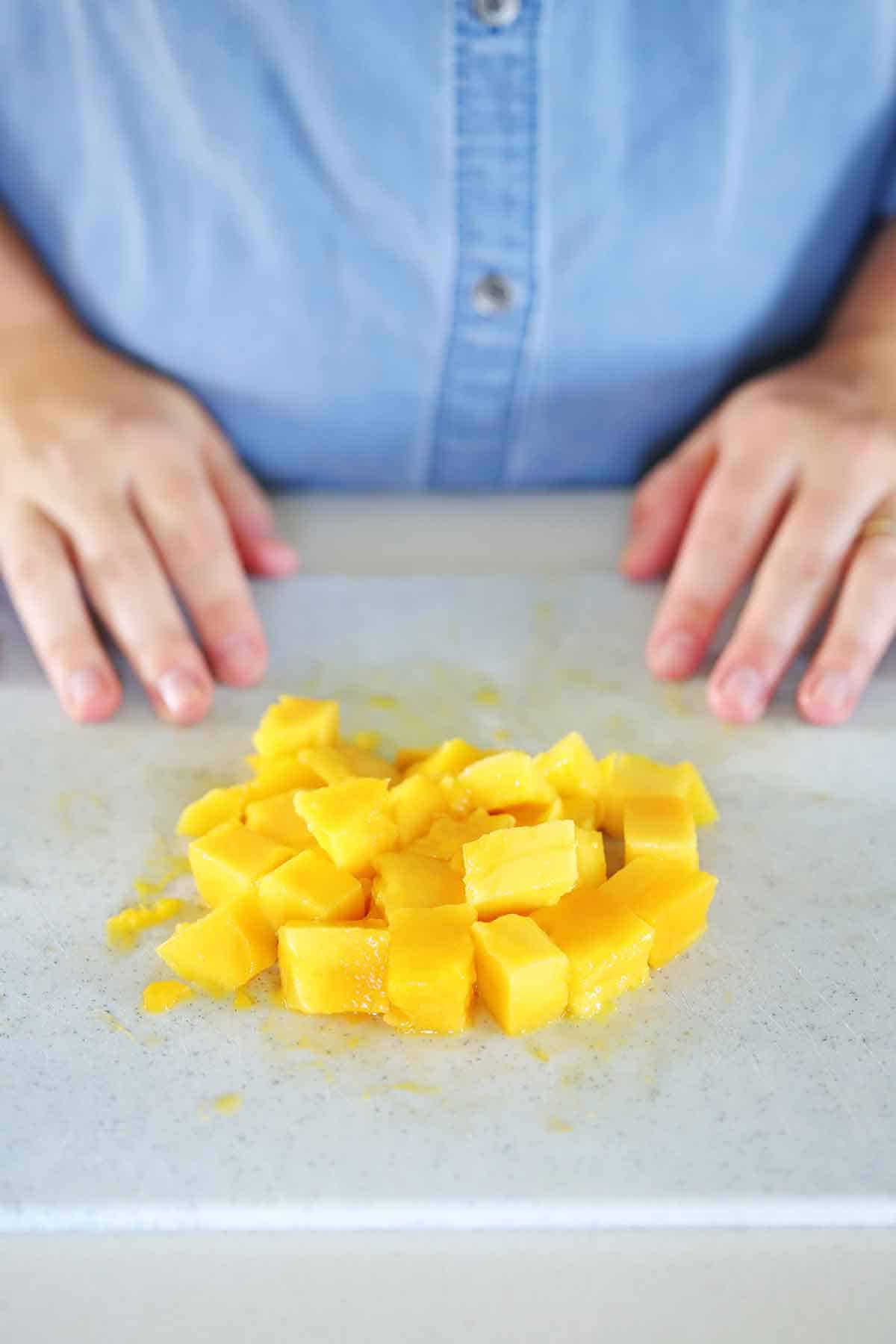 Cut mango on a cutting board with person behind it.