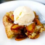 Close up photo of old-fashioned peach cobbler with vanilla ice cream melting on top.