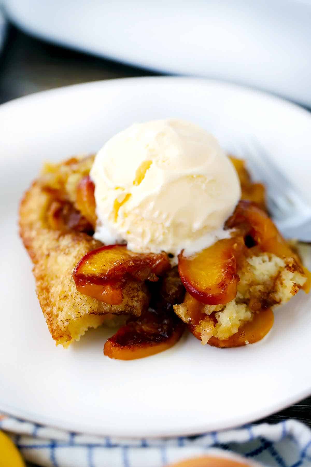 Close up photo of old-fashioned peach cobbler with vanilla ice cream melting on top.