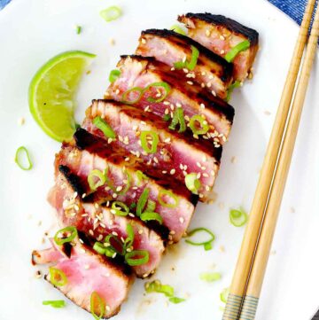 Square image of ahi tuna steaks sliced on a white plate with a lime wedge and chopsticks.