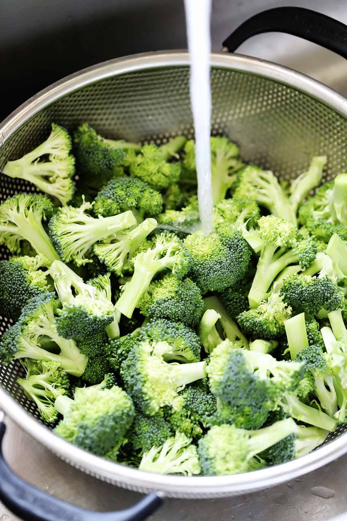 Washing broccoli in a colander.