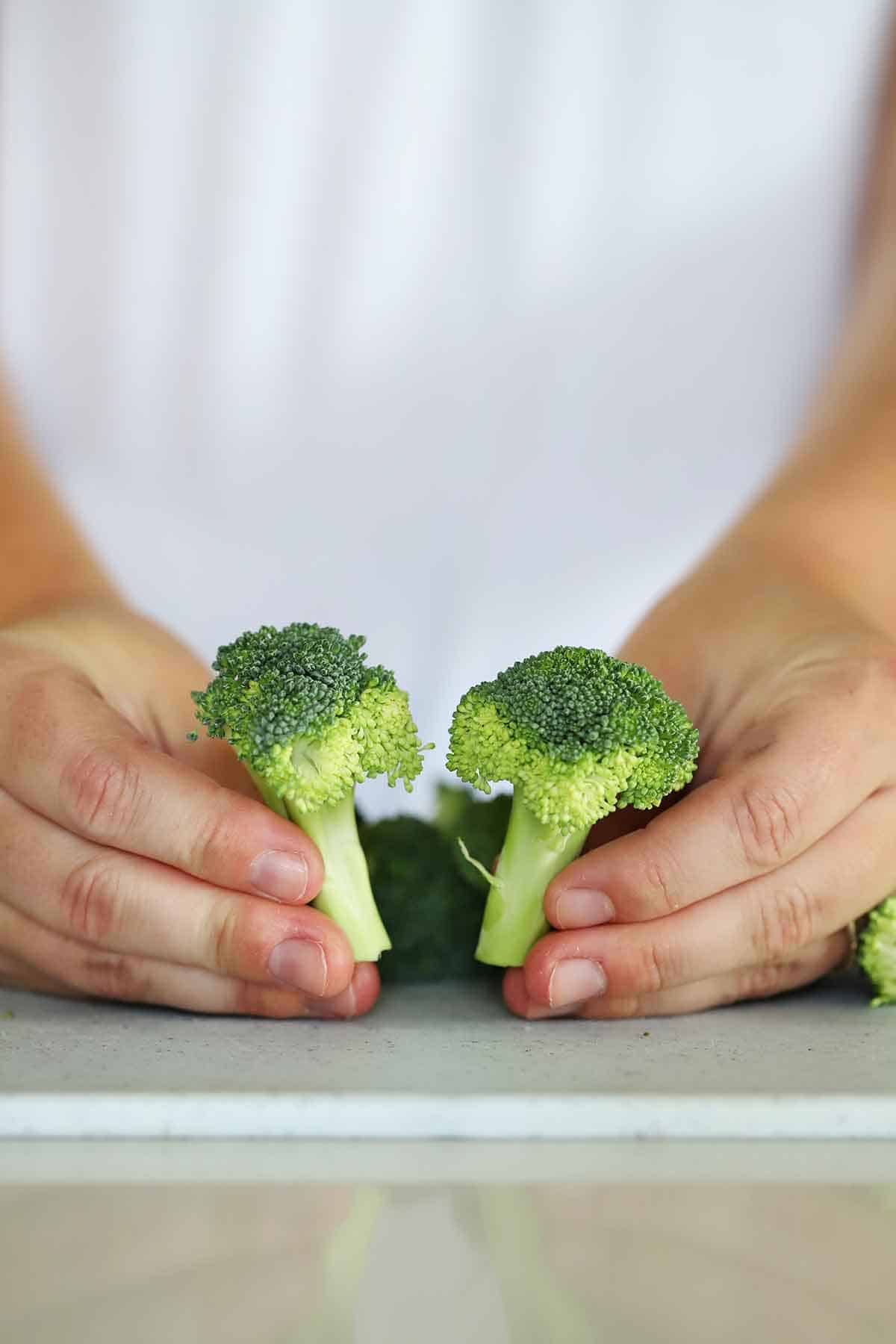Two large florets of broccoli being held.