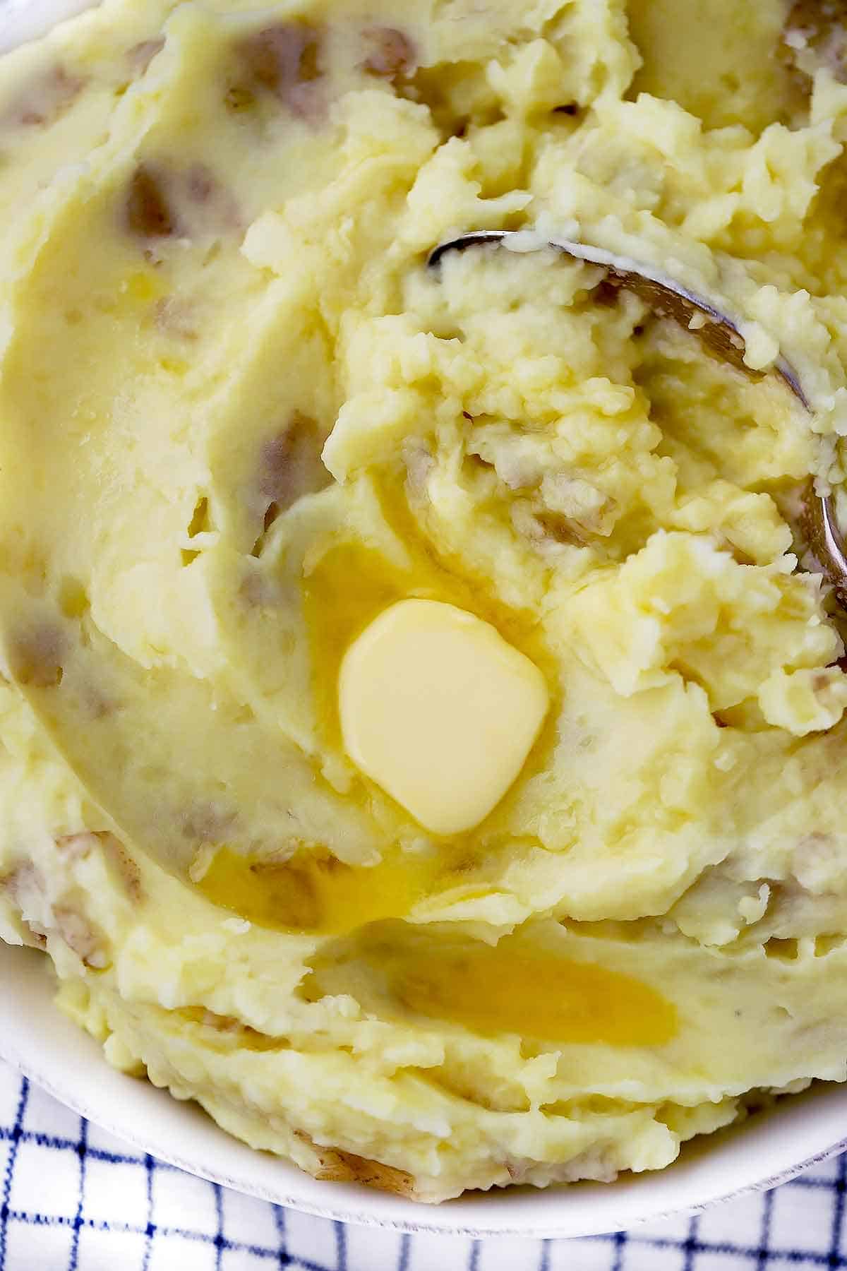 Close-up mashed potatoes with a pad of butter melting on top and a spoon.