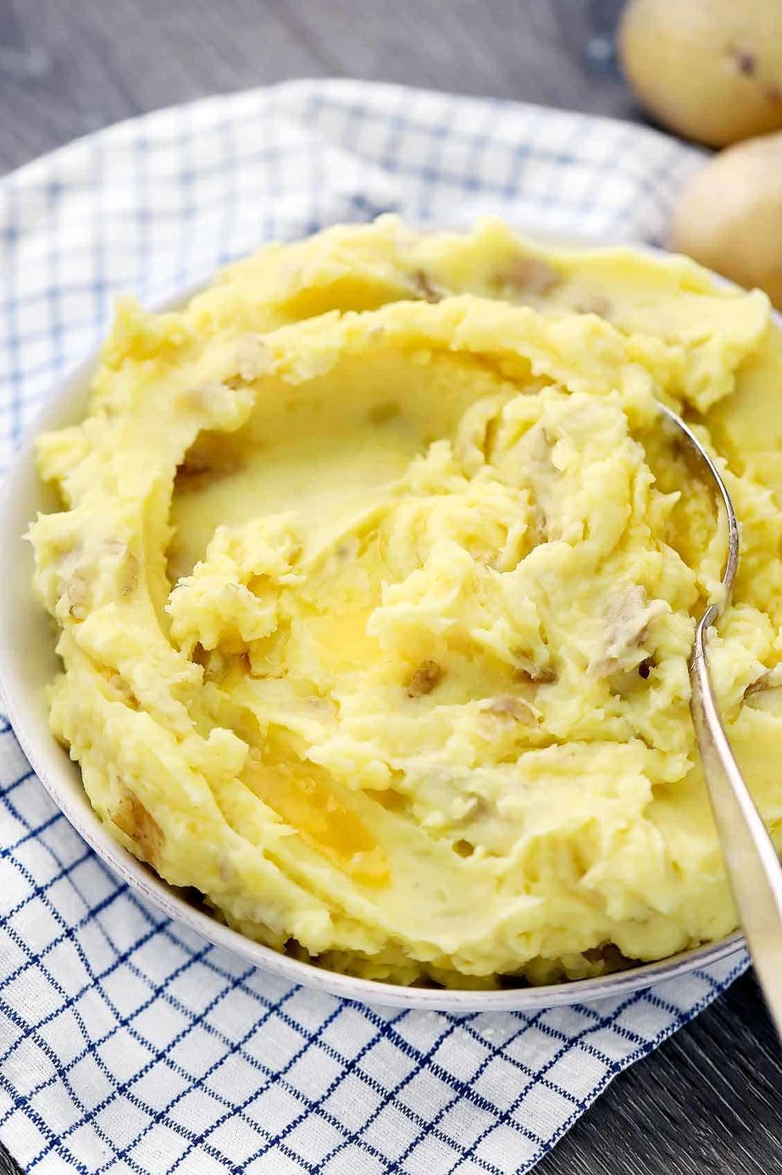 A bowl of homemade mashed potatoes with melted butter and a spoon.