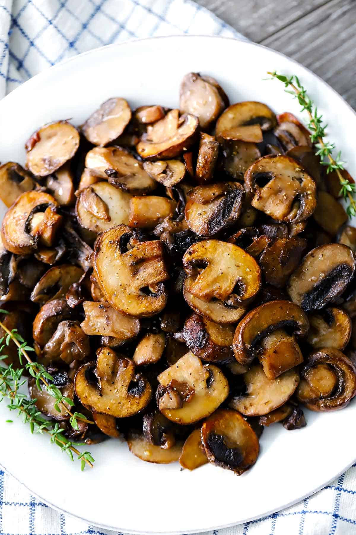 A white plate with sautéed mushrooms and sprigs of thyme.