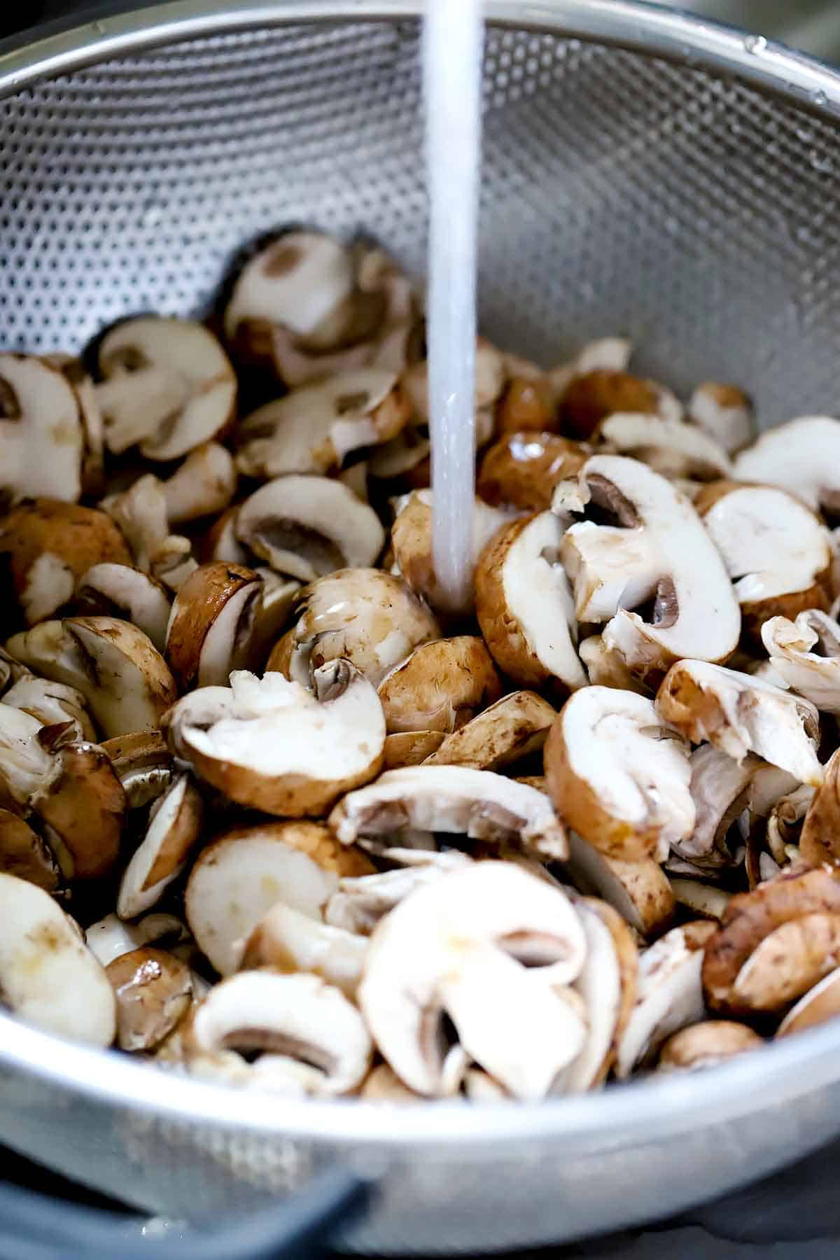 Washing sliced mushrooms in a colander.