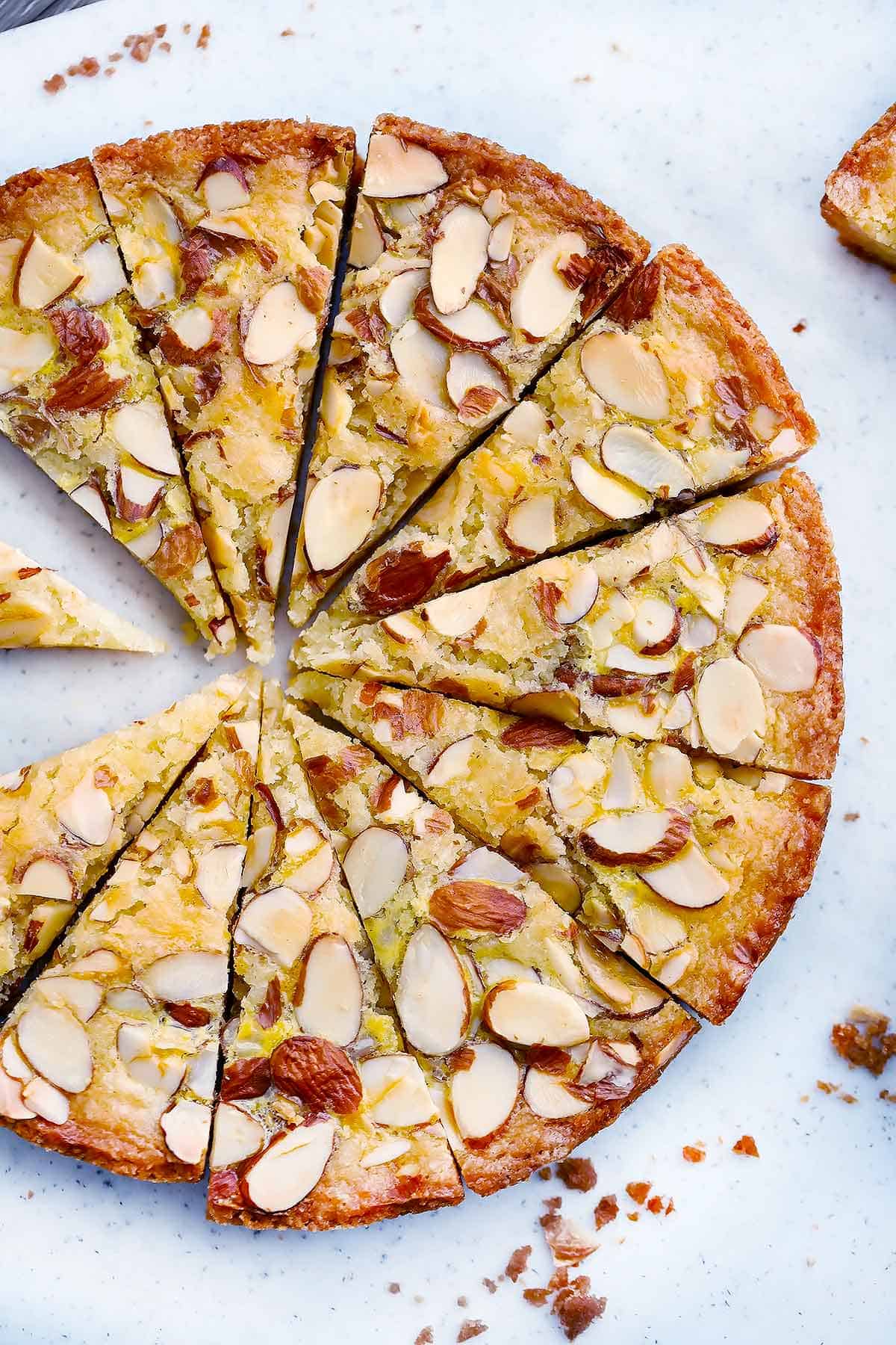 Dutch Butter Cake, or Boterkoek, on a cutting board, sliced into triangles, with sliced almonds on top.